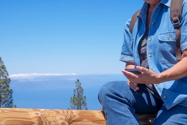 Foto mujer deportiva en excursión de montaña con mochila sentado en el tronco de un árbol mirando celular. horizonte sobre el mar en canarias