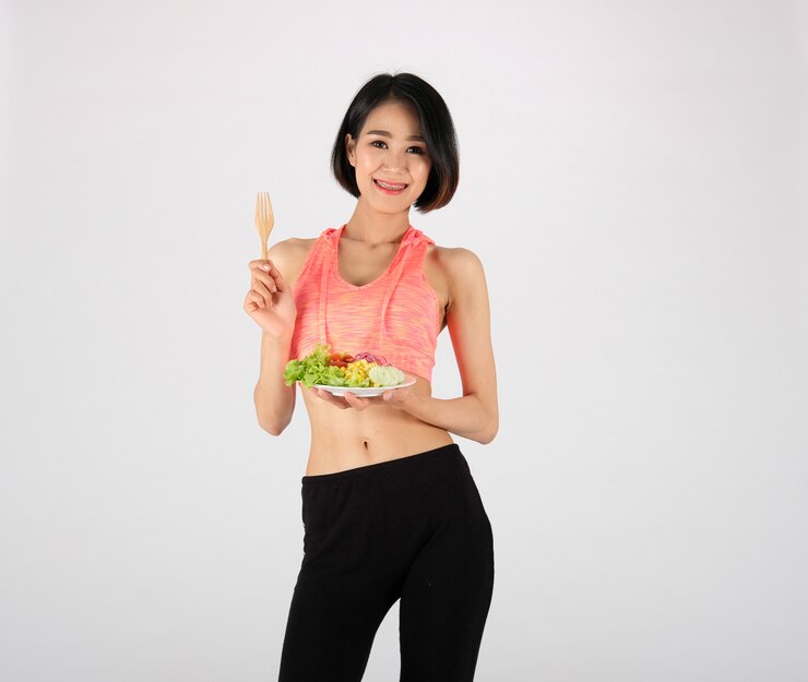 Mujer deportiva fitness en ropa deportiva con ensalada de verduras en blanco