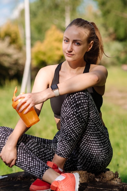 Una mujer deportiva en forma con una botella de agua se relaja después de los entrenamientos al aire libre