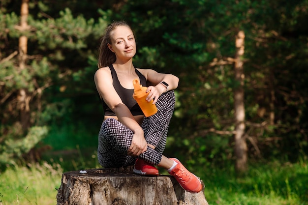 Una mujer deportiva en forma con una botella de agua se relaja después de los entrenamientos al aire libre