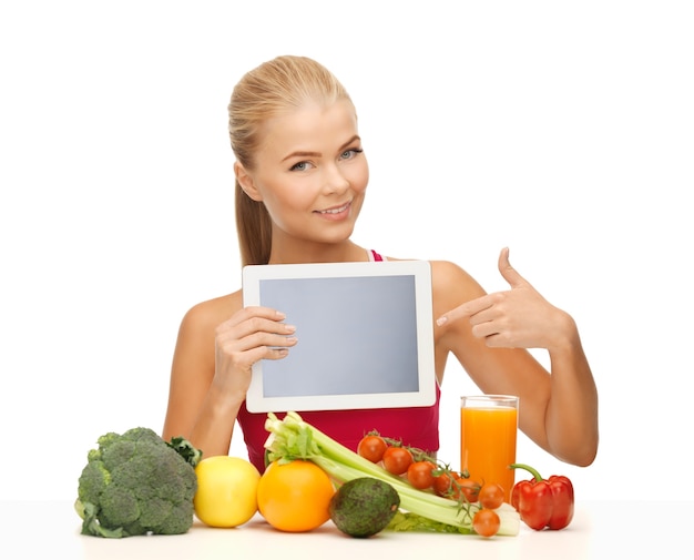 Mujer deportiva con frutas y verduras apuntando a tablet pc