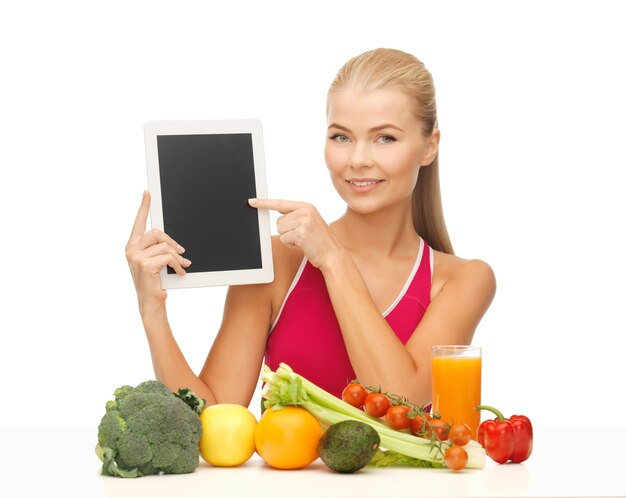 Mujer deportiva con frutas y verduras apuntando a tablet pc