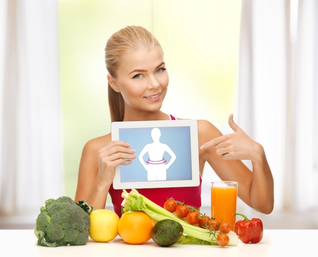 Mujer deportiva con frutas y verduras apuntando a tablet pc