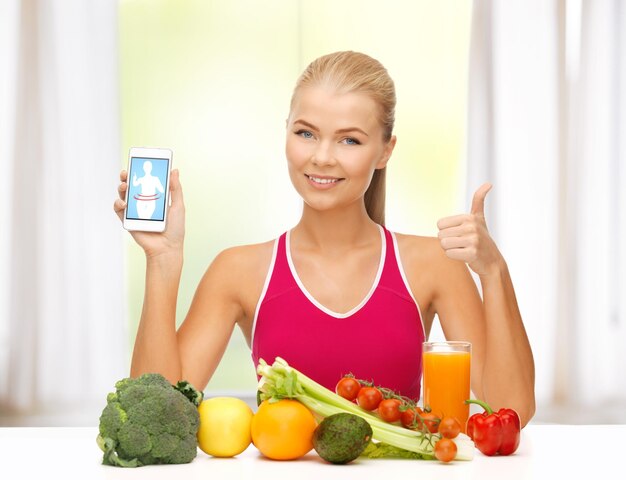 Mujer deportiva con frutas y verduras mostrando smartphone