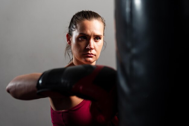 Una mujer deportiva con guantes de boxeo practica golpear una pera