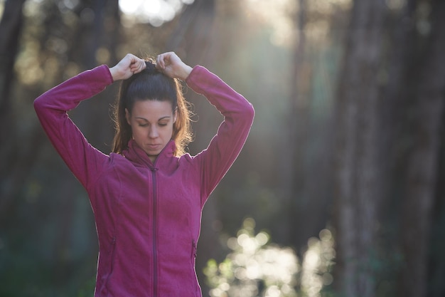 Mujer deportiva haciendo una cola de caballo con ropa deportiva en el bosque con rayo de sol y espacio para copiar