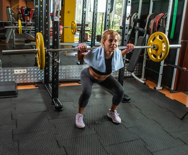 Mujer deportiva haciendo cuclillas con una barra en el gimnasio