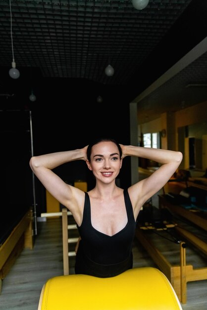 Mujer deportiva haciendo ejercicio de tonificación de pilates en la máquina de entrenamiento de barril de escalera de pilates de yoga trabajando en...