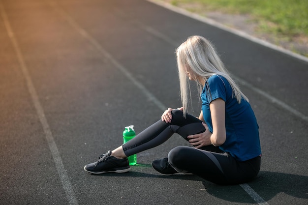 Mujer deportiva con lesión en el tobillo en pista de atletismo, concepto de salud y deporte. botella deportiva verde para beber