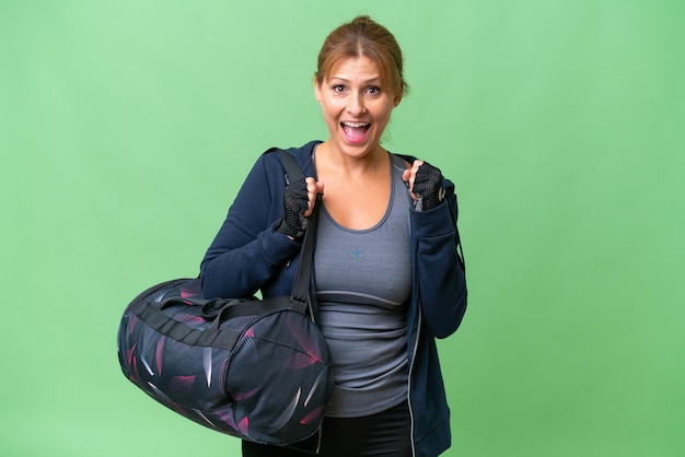 Mujer deportiva de mediana edad con bolsa deportiva sobre un fondo aislado celebrando una victoria en posición ganadora