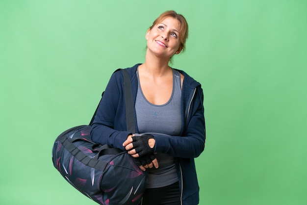 Mujer deportiva de mediana edad con bolsa deportiva sobre un fondo aislado mirando hacia arriba mientras sonríe