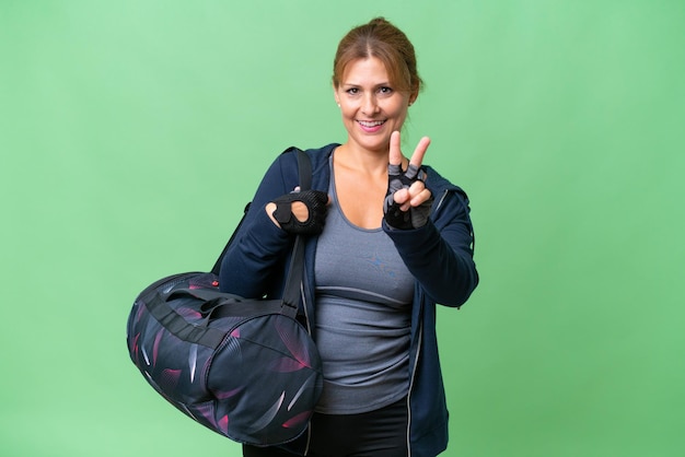 Mujer deportiva de mediana edad con bolsa deportiva sobre un fondo aislado sonriendo y mostrando el signo de la victoria