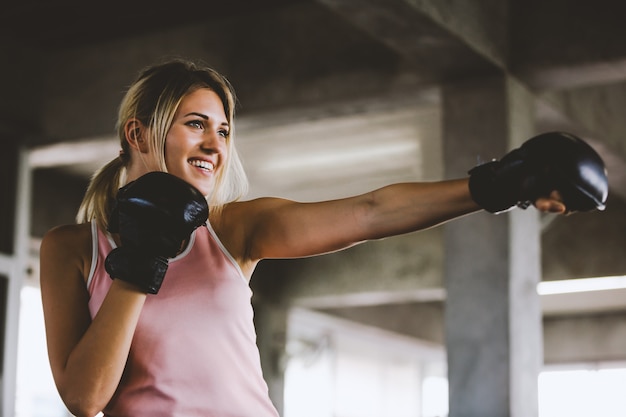 Mujer deportiva de la muchacha hermosa del retrato con los guantes de boxeo traseros que entrena en el gimnasio