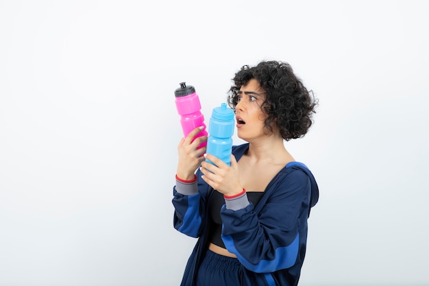 Mujer deportiva de pelo corto rizado con botellas de agua de color rosa y azul de pie.