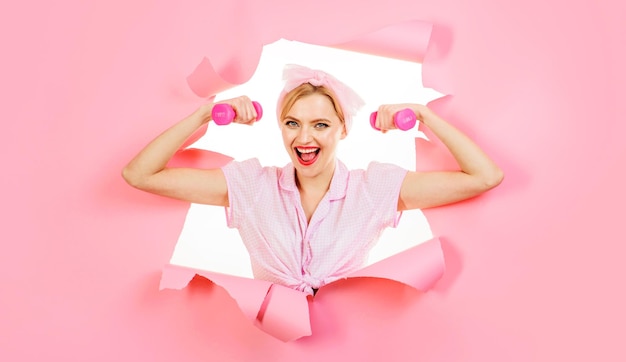 Mujer deportiva con pesas mirando a través del agujero de papel chica fitness con equipamiento deportivo