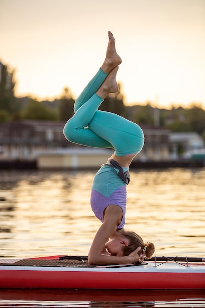 Mujer deportiva en posición de yoga en paddleboard, haciendo yoga en tabla de sup, ejercicio de flexibilidad y estiramiento de los músculos