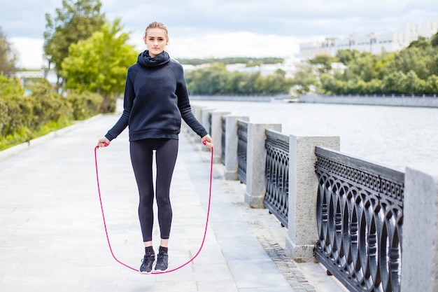 Mujer deportiva que calienta con la comba al aire libre.