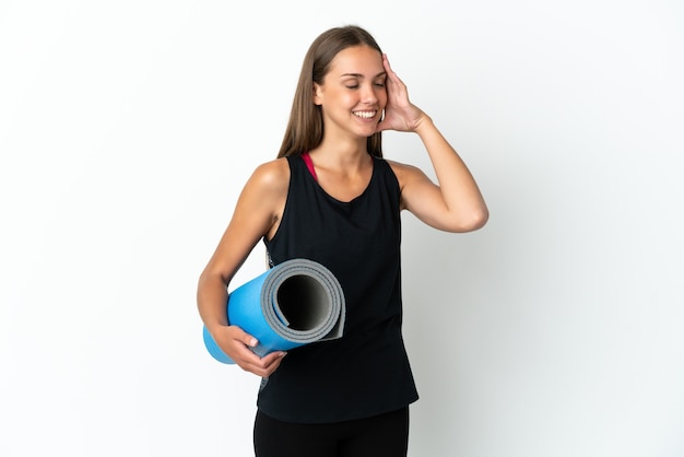 Mujer deportiva que va a clases de yoga mientras sostiene una estera sobre fondo blanco aislado sonriendo mucho