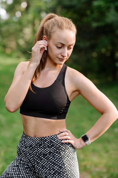 Mujer deportiva en ropa deportiva con auriculares durante los ejercicios matutinos en el parque