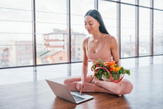 Mujer deportiva sentada en la mesa con laptop y comida saludable.