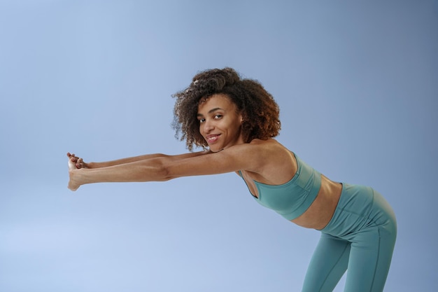 Mujer deportiva sonriente haciendo calentamiento antes de la sesión de entrenamiento en el gimnasio en el fondo del estudio