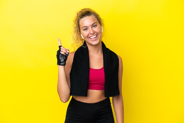 Mujer deportiva con toalla aislada de fondo amarillo mostrando y levantando un dedo en señal de lo mejor