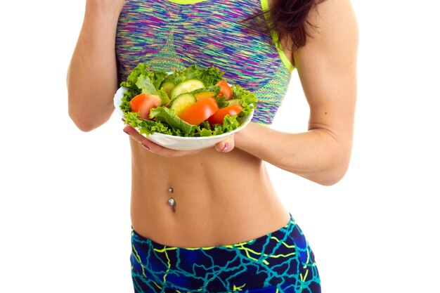 Mujer deportiva en top deportivo de colores y leggins con plato blanco con ensalada verde y tomate