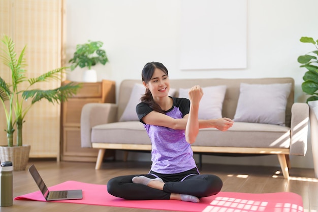 Mujer deportiva viendo entrenamiento de yoga en línea y estirando los brazos para hacer ejercicio de yoga en casa