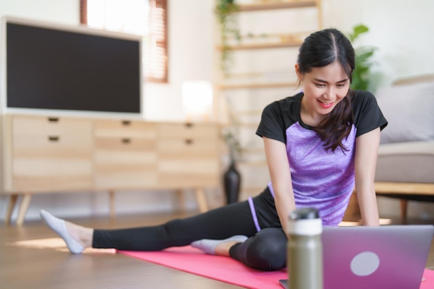 Mujer deportiva viendo entrenamiento de yoga en línea y estirando las piernas para hacer ejercicio de yoga en casa