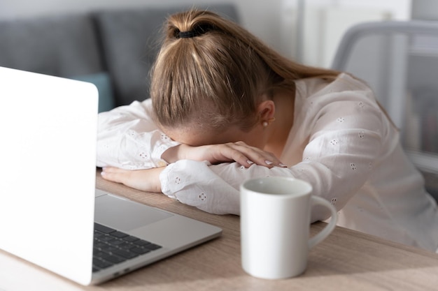 Mujer deprimida con la cabeza en el escritorio frente a la computadora portátil Concepto de ansiedad y depresión en el trabajo