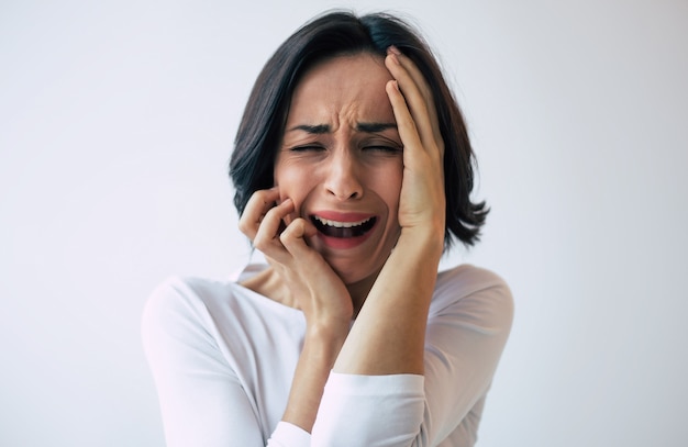 Mujer deprimida con corte de pelo corto que llora mientras se toca la cara. Niña que grita con los ojos cerrados debido a su enfermedad mental.