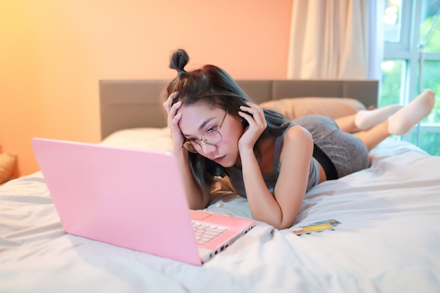 Mujer deprimida y estresada acostada con computadora y tarjeta de crédito en el dormitorio