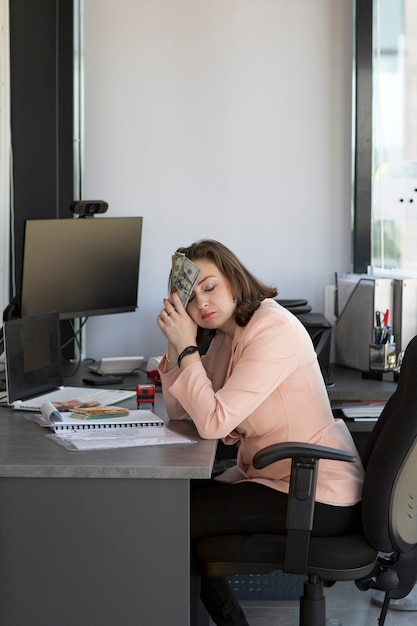 Mujer deprimida que cubre su rostro por las manos en la oficina con dinero en billetes de dólares estadounidenses en su rostro. Triste mujer preocupada y desesperada banca y contabilidad. concepto de finanzas, ahorro y banca