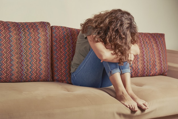 Foto la mujer deprimida se sienta en el sofá en la sala de estar. mujer triste y solitaria agacha la cabeza. concepto de depresión y estrés