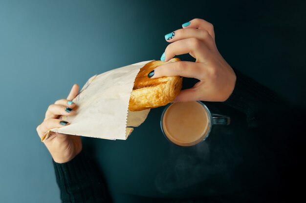 Mujer desayunando croissant francés y café en una mesa oscura