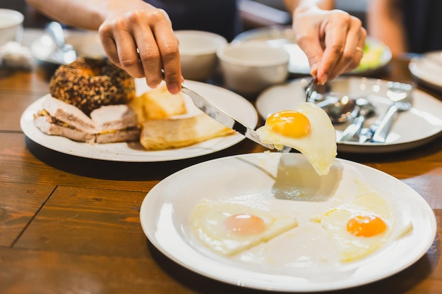 Mujer desayunando huevos fritos con amigos en una mesa de madera