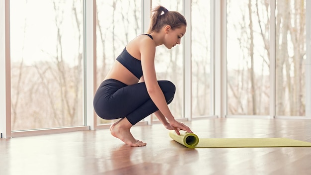 Mujer descalza estera rodante después del entrenamiento de yoga