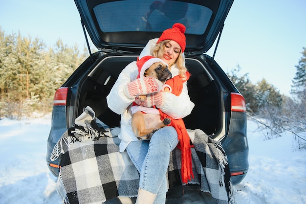 Mujer descansando en el bosque de invierno sentada en el maletero abierto de un coche con un perro.