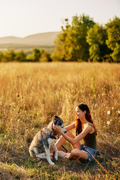 Una mujer descansando después de un paseo se sienta en un campo con un perro salchicha sonriendo mientras pasa tiempo al aire libre con un perro amigo en otoño al atardecer durante el viaje