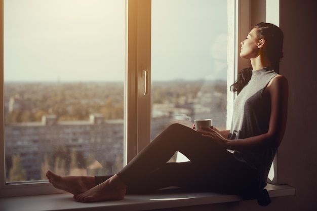 Mujer descansando y pensando con los ojos cerrados. Chica tranquila con taza de té o café sentado en el