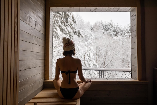 Mujer descansando en la sauna con vistas a la naturaleza nevada