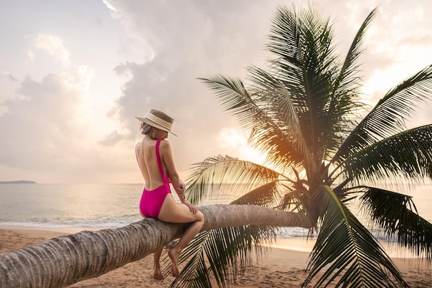 Mujer descansando sobre una palmera de coco inclinada