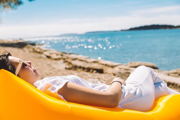 Foto mujer descansando en un sofá de aire inflable amarillo en la playa del mar en un día soleado de vacaciones de verano