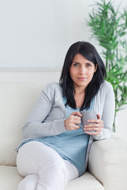 Mujer descansando en un sofá mientras sostiene una taza gris