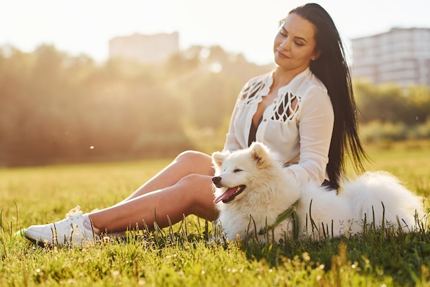 Mujer descansando en el suelo del campo con su lindo perro blanco