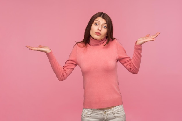 Mujer desconcertada y confundida con suéter rosa encogiéndose de hombros desconcertada, dudando y sintiéndose insegura, no tiene idea Foto de estudio interior aislada en fondo rosa