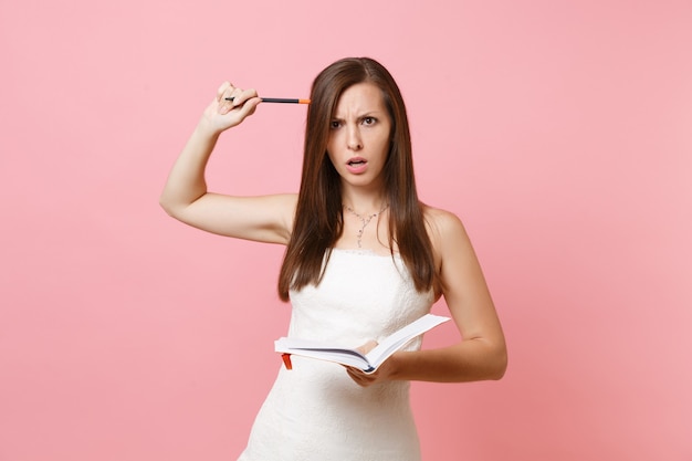 Mujer desconcertada en vestido blanco buscando ideas escribiendo notas en el cuaderno diario