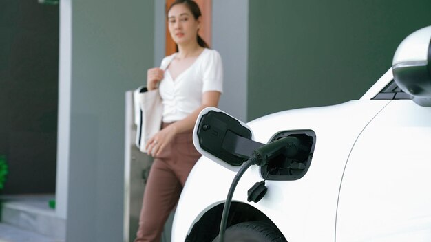 Foto una mujer desconecta el cargador del vehículo eléctrico en su residencia. el concepto de uso de vehículos eléctricos en un estilo de vida progresista contribuye a un medio ambiente limpio y saludable.