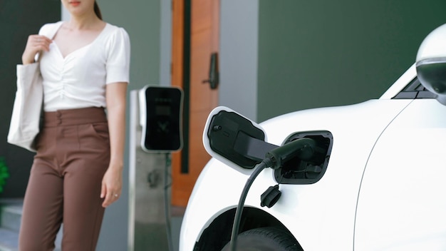 Una mujer desconecta el cargador del vehículo eléctrico en su residencia El concepto del uso de vehículos eléctricos en un estilo de vida progresivo contribuye a un medio ambiente limpio y saludable