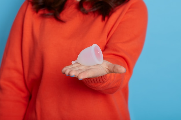 Mujer desconocida con cabello oscuro sosteniendo la copa menstrual en su palma, la niña sin rostro durante el período elige un producto higiénico para su propia seguridad